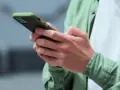 Dłonie trzymające smartfon w zielonym etui, gotowe na nowe powiadomienia push.