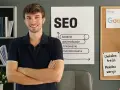 Uśmiechnięty mężczyzna stoi przed tablicą z hasłami SEO i Google. Jego **witryna internetowa** z pewnością będzie dobrze wypozycjonowana.