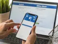 Ręce trzymają telefon z ekranem logowania Facebooka, obok laptopa. Zastanawiasz się, dlaczego strona na Facebooku jest niewidoczna?