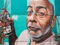 Mural przedstawiający mężczyznę z wąsami i okularami, trzymającego puszkę farby. To przykład odważnego guerrilla marketing.