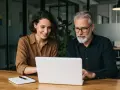 Dwóch współpracowników analizuje dane na laptopie, dyskutując o tym, saas co to jest i jak może usprawnić ich pracę.