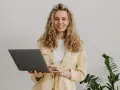 Uśmiechnięta kobieta z kręconymi włosami trzyma laptopa. To nasz przykład, jak pracujemy.