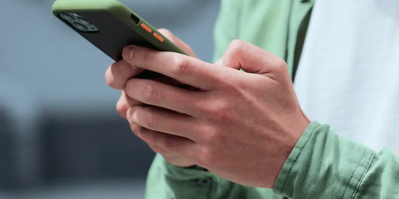 Dłonie trzymające smartfon w zielonym etui, gotowe na nowe powiadomienia push.