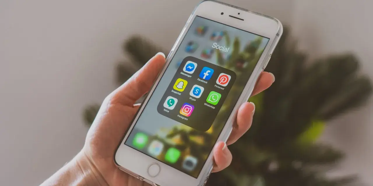 Dłoń trzyma smartfon z ikonami aplikacji społecznościowych. Chcesz wiedzieć, jak promować post na Instagramie? Zacznij od tych narzędzi!