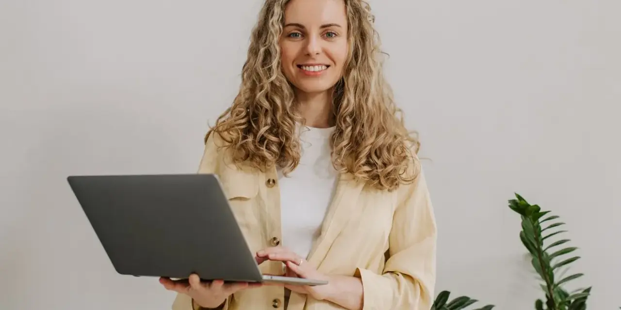 Uśmiechnięta kobieta z kręconymi włosami trzyma laptopa. To nasz przykład, jak pracujemy.