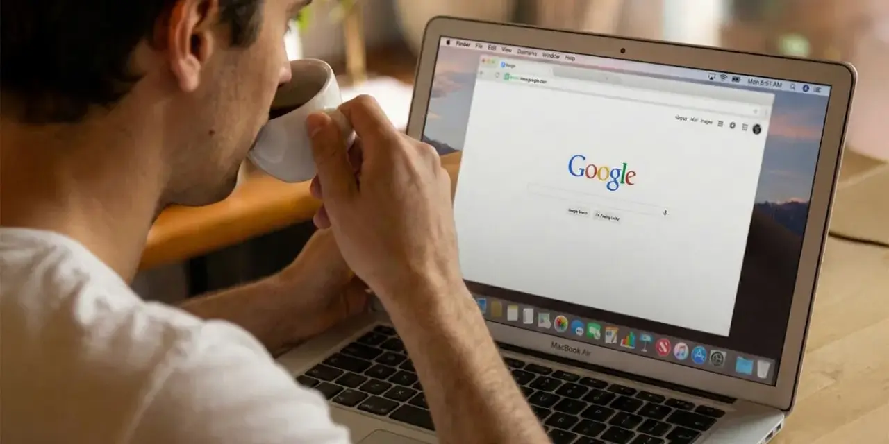 Mężczyzna popija kawę, przeglądając stronę Google na laptopie. Dyskutuje o aktualizacjach algorytmu Google.