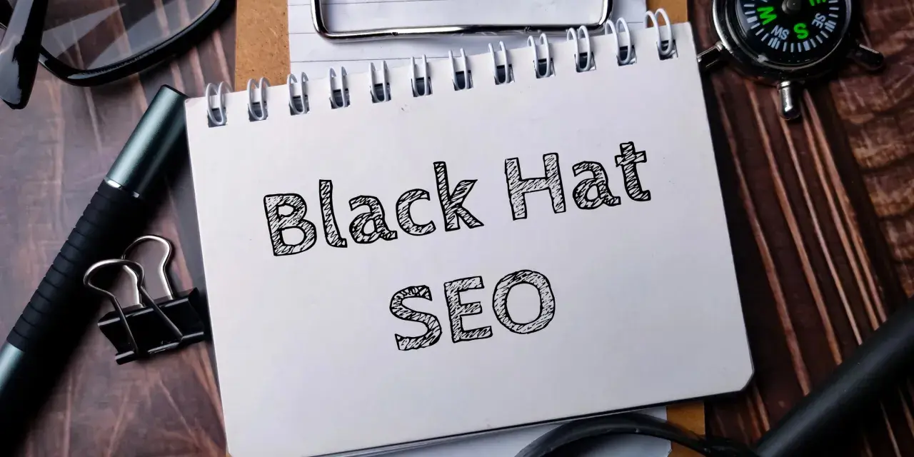 Notatnik z napisem "Black Hat SEO", okulary, długopis i kompas na drewnianym tle.