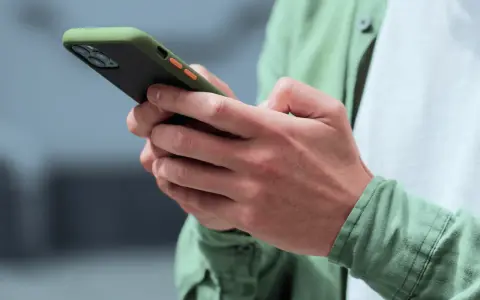 Dłonie trzymające smartfon w zielonym etui, gotowe na nowe powiadomienia push.