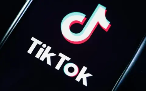 Logo TikToka na czarnym tle. Aplikacja zyskała popularność w 2018 roku, choć jej początki sięgają 2016.