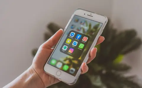 Dłoń trzyma smartfon z ikonami aplikacji społecznościowych. Chcesz wiedzieć, jak promować post na Instagramie? Zacznij od tych narzędzi!