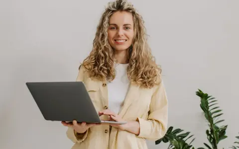 Uśmiechnięta kobieta z kręconymi włosami trzyma laptopa. To nasz przykład, jak pracujemy.