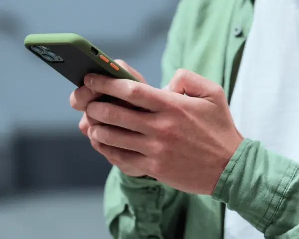 Dłonie trzymające smartfon w zielonym etui, gotowe na nowe powiadomienia push.