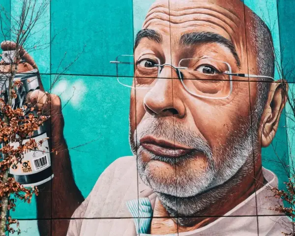 Mural przedstawiający mężczyznę z wąsami i okularami, trzymającego puszkę farby. To przykład odważnego guerrilla marketing.