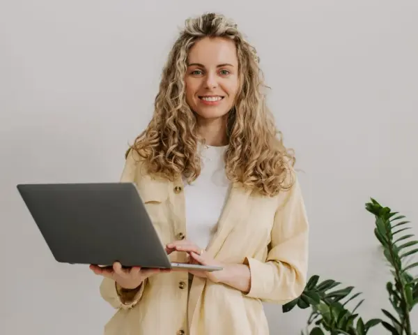 Uśmiechnięta kobieta z kręconymi włosami trzyma laptopa. To nasz przykład, jak pracujemy.