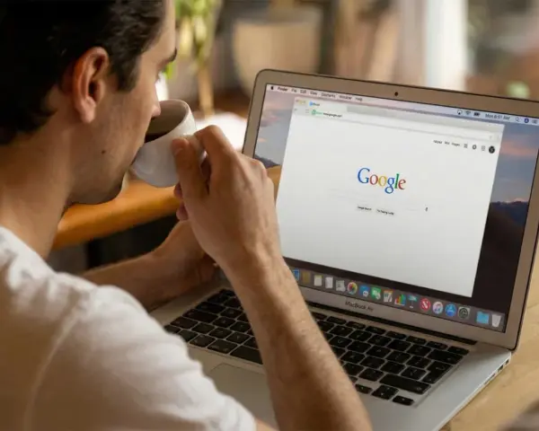 Mężczyzna popija kawę, przeglądając stronę Google na laptopie. Dyskutuje o aktualizacjach algorytmu Google.