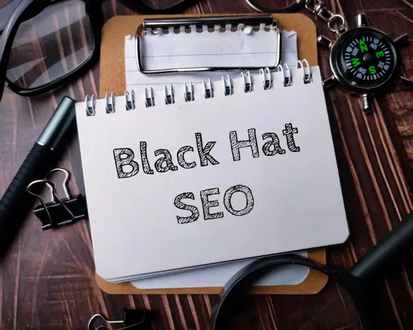 Notatnik z napisem "Black Hat SEO", okulary, długopis i kompas na drewnianym tle.