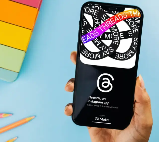 Dłoń trzyma smartfon z aplikacją Threads, która pozwala dzielić się pomysłami i trendami.