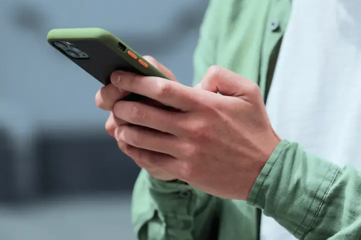 Dłonie trzymające smartfon w zielonym etui, gotowe na nowe powiadomienia push.