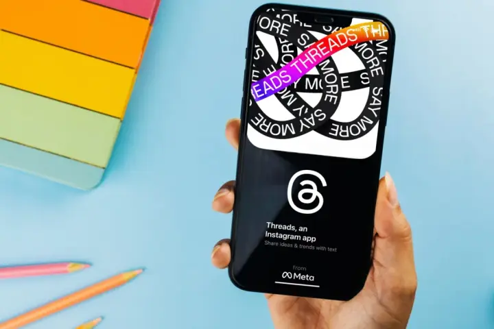 Dłoń trzyma smartfon z aplikacją Threads, która pozwala dzielić się pomysłami i trendami.