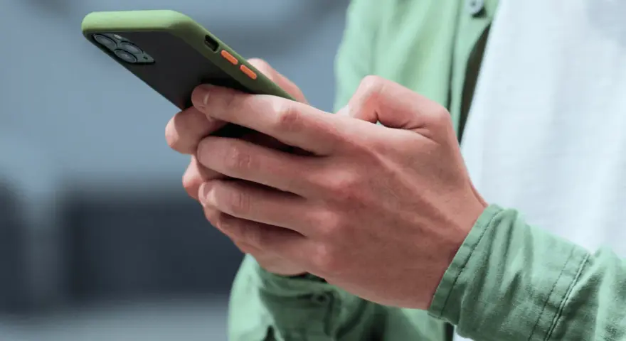 Dłonie trzymające smartfon w zielonym etui, gotowe na nowe powiadomienia push.