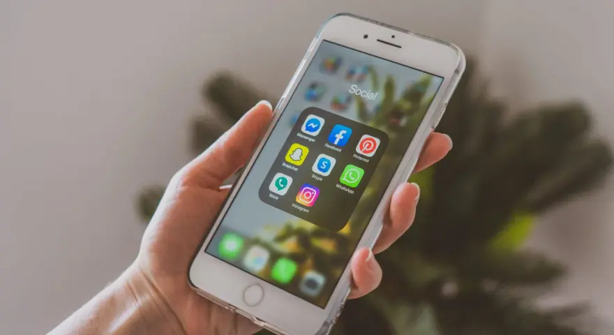 Dłoń trzyma smartfon z ikonami aplikacji społecznościowych. Chcesz wiedzieć, jak promować post na Instagramie? Zacznij od tych narzędzi!