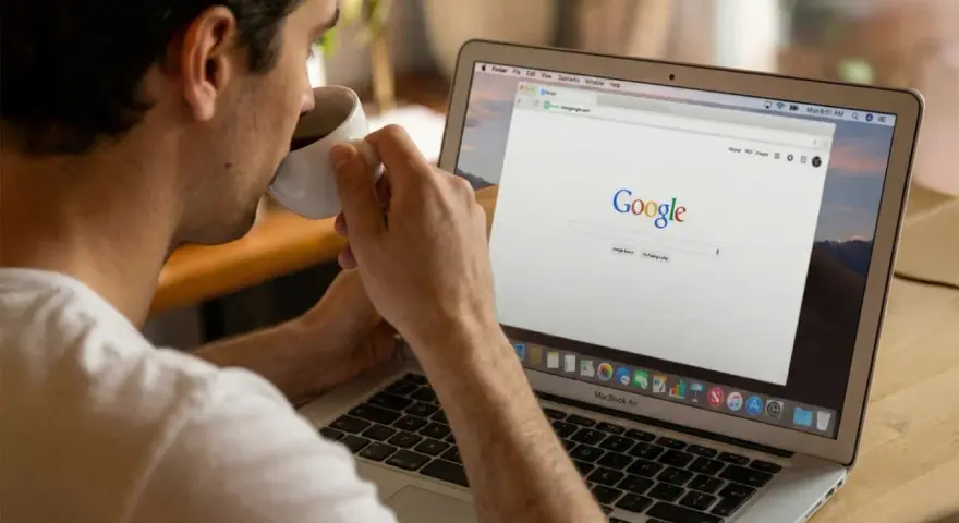 Mężczyzna popija kawę, przeglądając stronę Google na laptopie. Dyskutuje o aktualizacjach algorytmu Google.