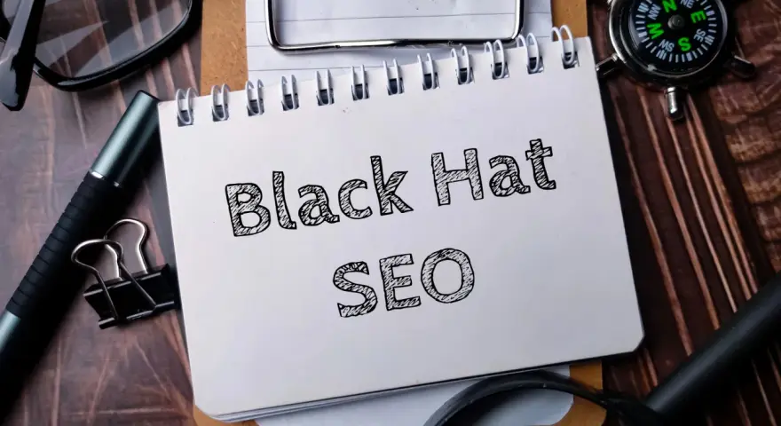 Notatnik z napisem "Black Hat SEO", okulary, długopis i kompas na drewnianym tle.