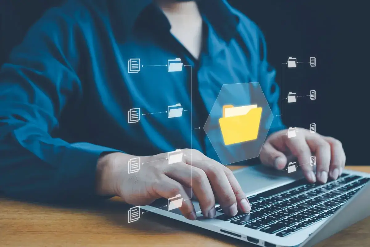 Osoba pracuje na laptopie, a na ekranie widoczne są ikony folderów i dokumentów, symbolizujące archiwum stron internetowych.
