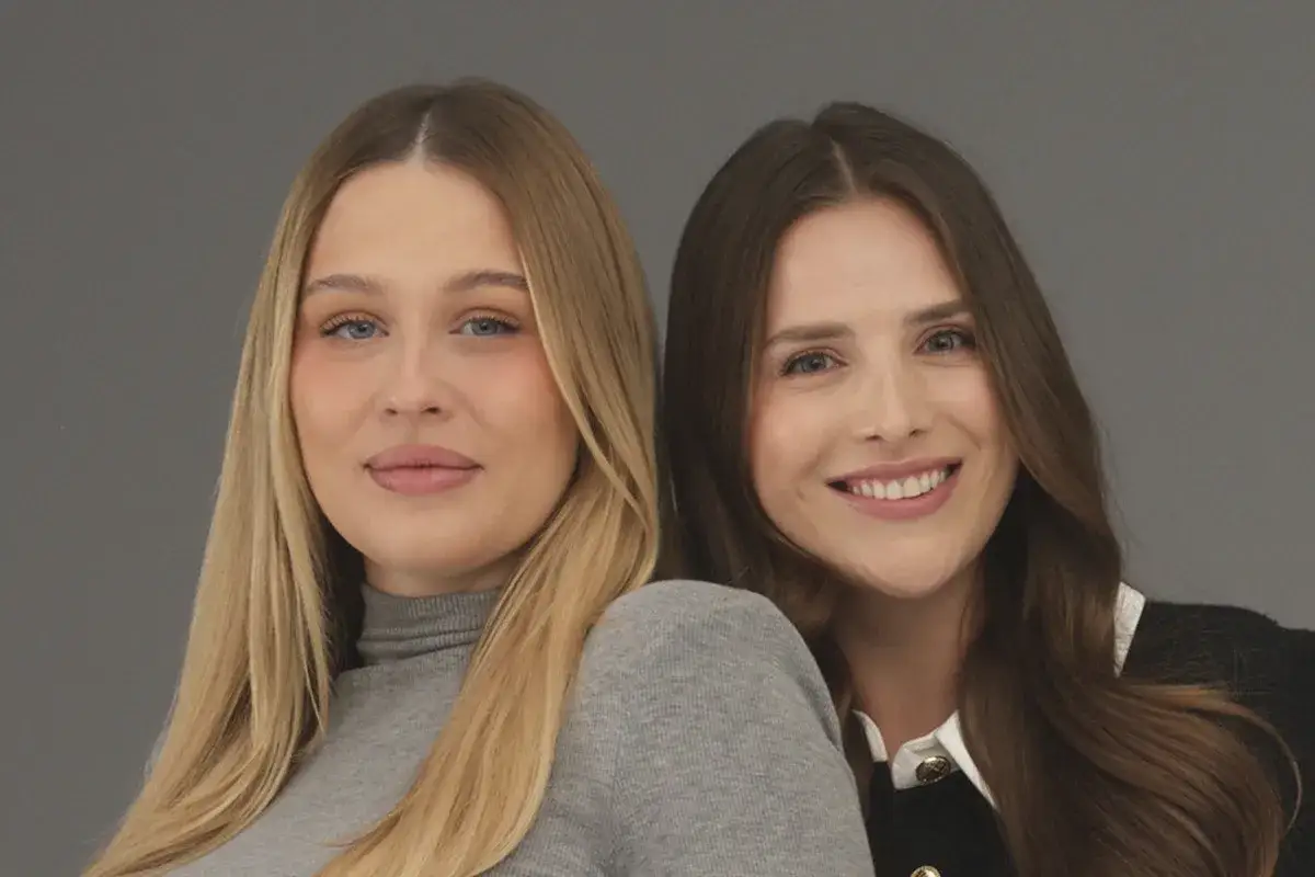 Dwie uśmiechnięte polskie influencerki, jedna z blond włosami w szarym golfie, druga z brązowymi włosami w czarnej bluzce.